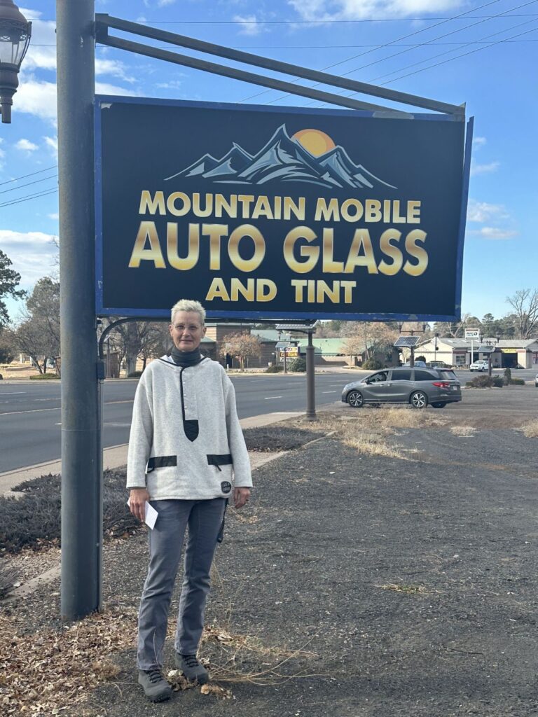 Lady-$500 Winner Lady in white sweater with $500 check by the Mountain Mobile Auto Glass And Tint sign.